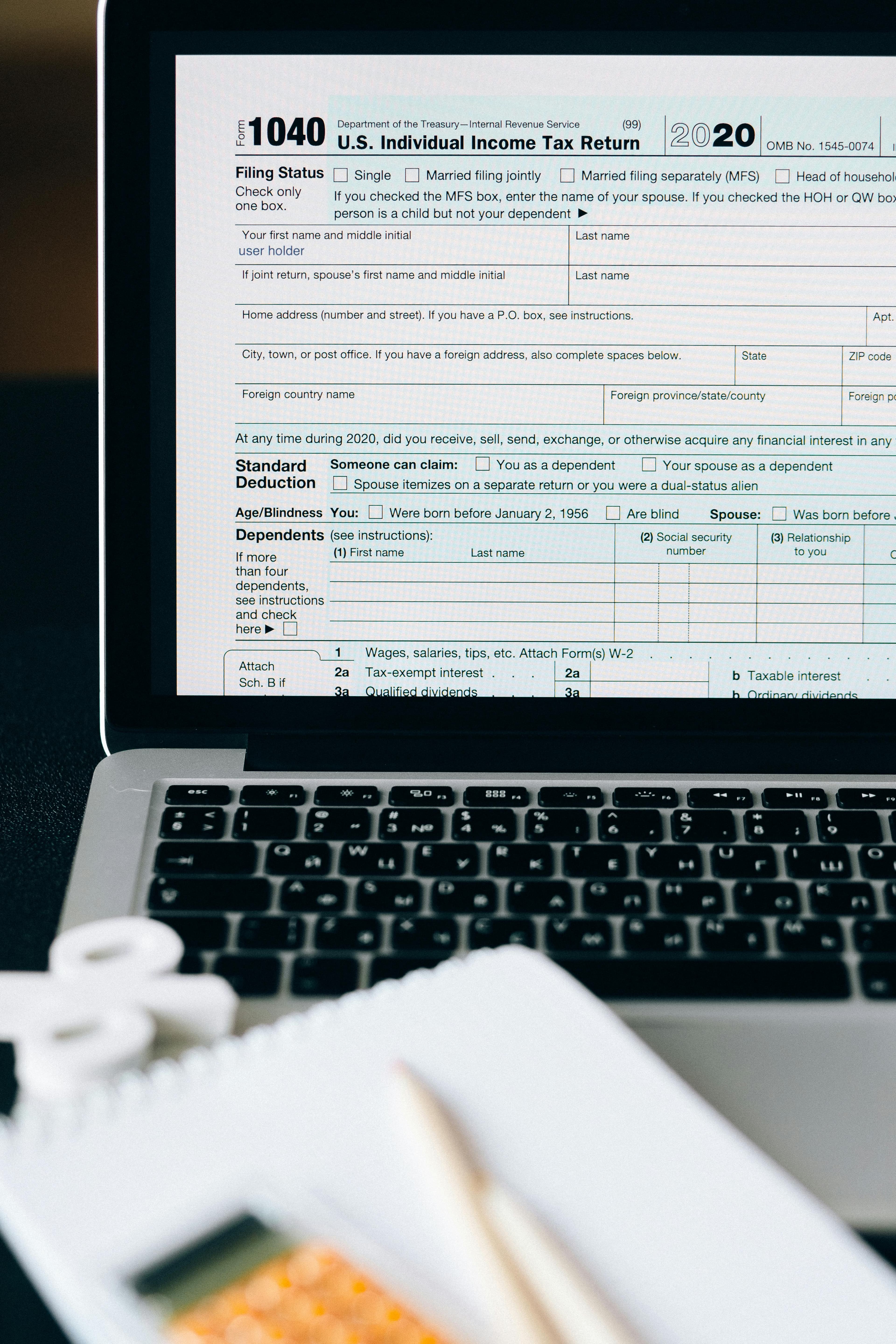Laptop displaying a Form 1040 tax return alongside a calculator